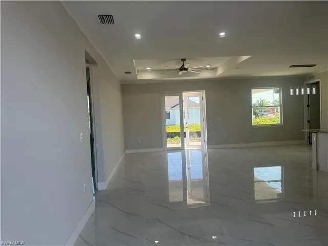 Spare room with a tray ceiling, tile flooring, plenty of natural light, and ceiling fan