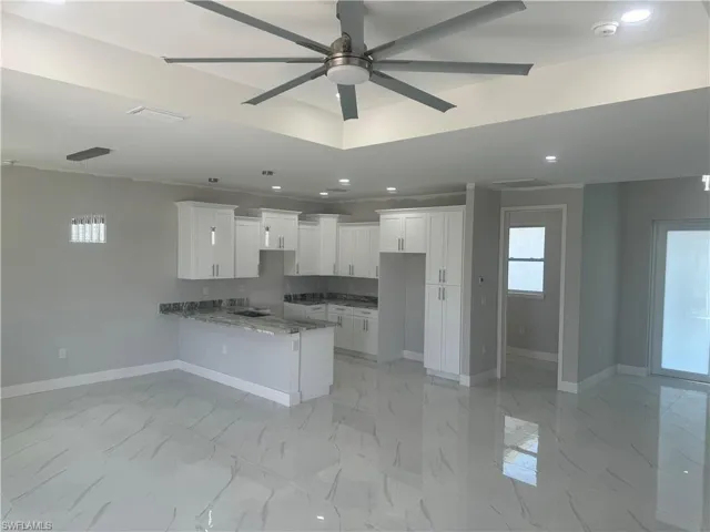 Kitchen with light stone countertops, ceiling fan, kitchen peninsula, light tile floors, and white cabinetry