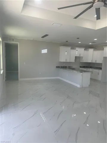 Kitchen featuring ceiling fan, light stone counters, white cabinetry, and light tile floors