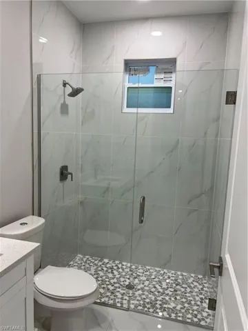 Bathroom featuring a shower with shower door, tile flooring, vanity, and toilet