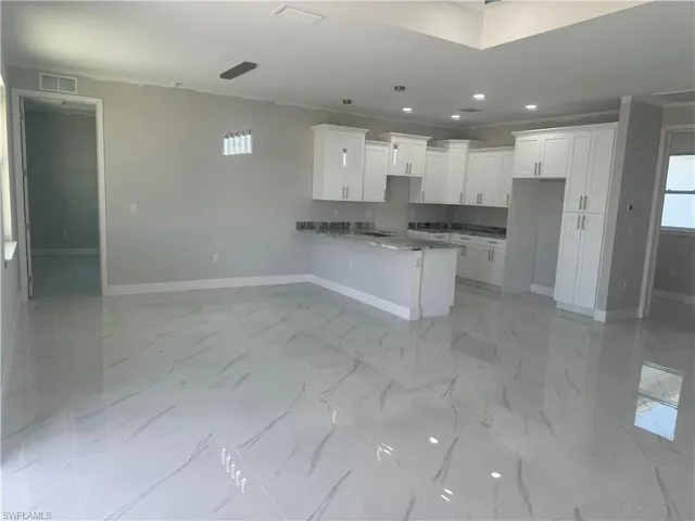 Kitchen with kitchen peninsula, pendant lighting, light stone counters, light tile floors, and white cabinets