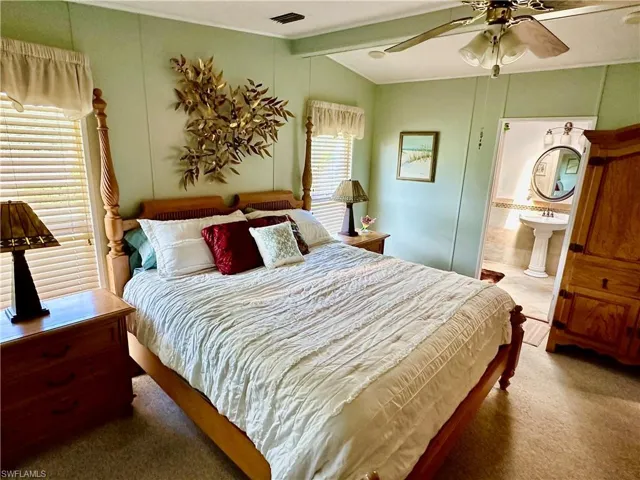 Carpeted bedroom with lofted ceiling with beams, ensuite bathroom, and mirror closet doors