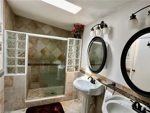 Master bathroom featuring a walk in shower with tiled seat, pedestal sinks, and tile patterned flooring and walls