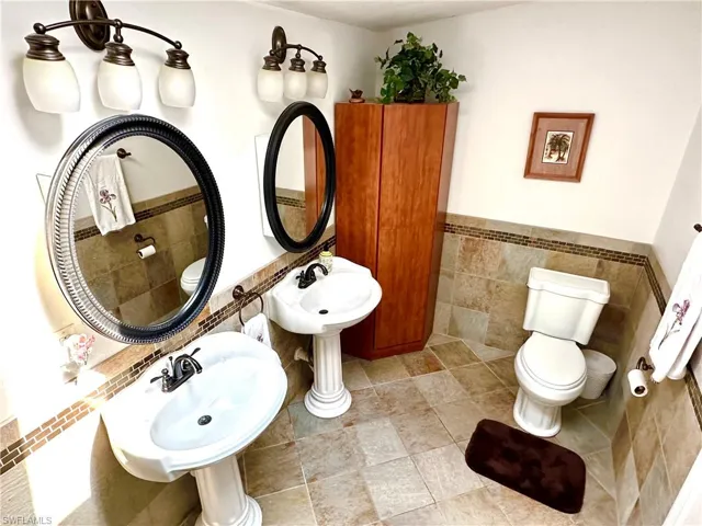 Bathroom featuring walk in shower pedestal sinks, and tile walls