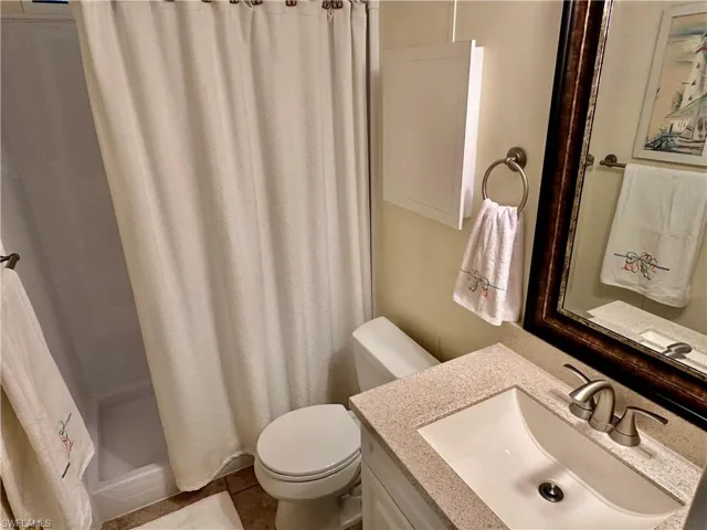 Bathroom with corin counter top vanity, toilet, tile patterned floors, and a shower with curtain
