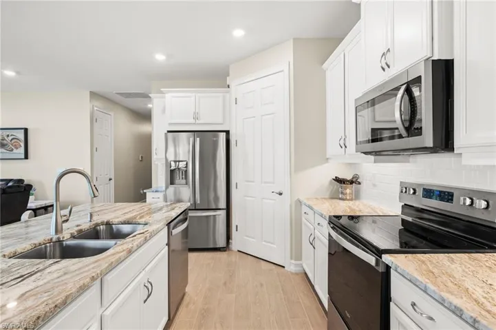 Kitchen with appliances with stainless steel finishes, white cabinetry, decorative backsplash, light wood finished floors, and recessed lighting