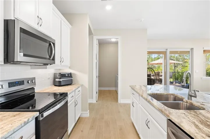 Kitchen featuring appliances with stainless steel finishes, backsplash, white cabinets, light wood finished floors, and light stone counters