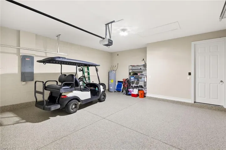 Garage featuring electric panel, water heater, a garage door opener, and concrete block wall
