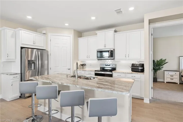 Kitchen featuring appliances with stainless steel finishes, light wood-style flooring, a kitchen bar, white cabinets, and recessed lighting