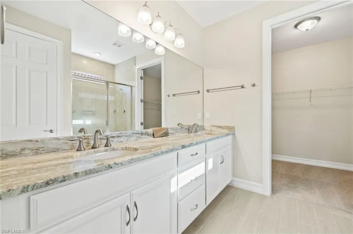 Full bath with a shower stall, double vanity, and a spacious closet