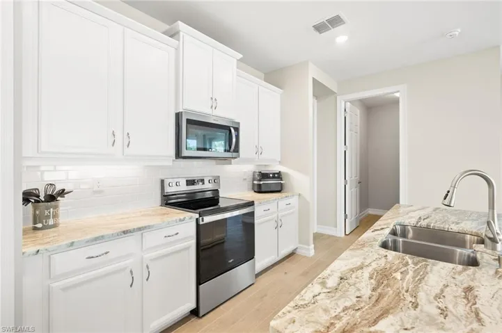 Kitchen featuring appliances with stainless steel finishes, backsplash, light wood-type flooring, white cabinetry, and light stone counters