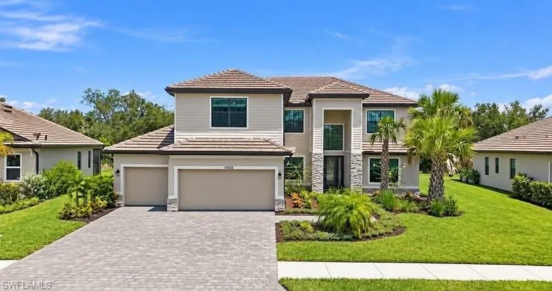 Two-story stucco exterior with stone accents, featuring a multi-car garage, paver driveway, and mature landscaping