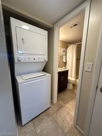 Clothes washing area featuring stacked washer and clothes dryer and light tile patterned floors
