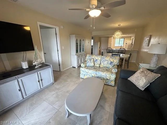 Living room featuring light tile patterned flooring and ceiling fan with notable chandelier