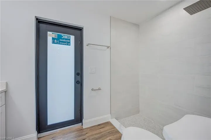 Walk-in shower featuring large-format wall tile, a rainfall showerhead, and a mosaic tile floor, paired with a dark-framed frosted glass exterior door and wood-finish flooring