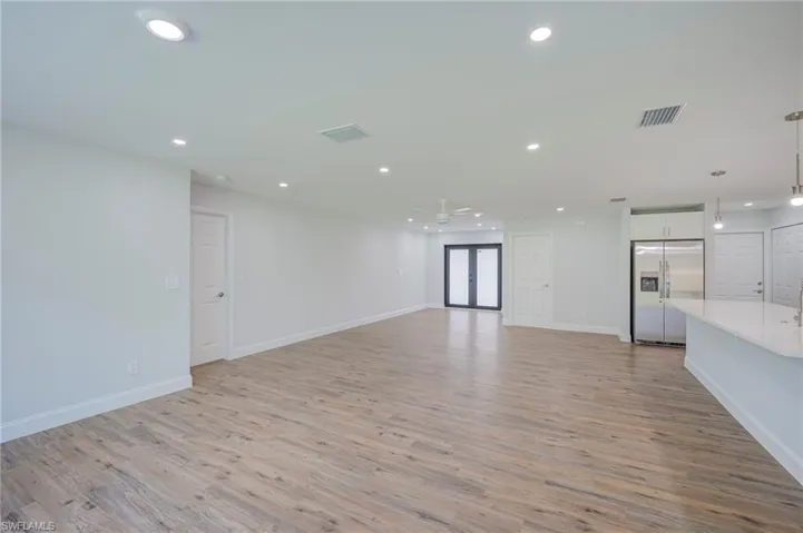 Open-concept interior featuring wood-finish flooring, recessed lighting, double glass-panel doors, and an expansive quartz-surface island