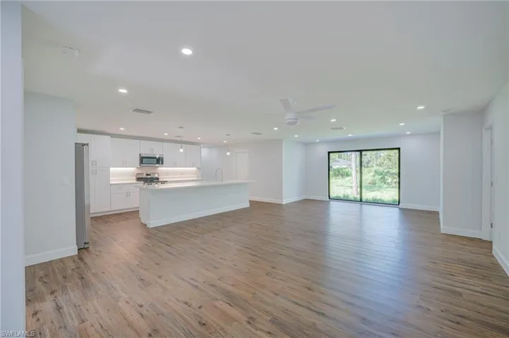 Open-concept space featuring wood-finish flooring, white cabinetry, a center island with quartz countertops, recessed lighting, and sliding glass doors