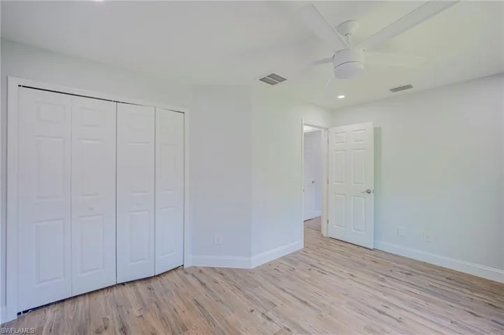 Interior space featuring wood-finish flooring, a white six-panel door, bifold closet doors, and a ceiling-mounted fan with integrated lighting