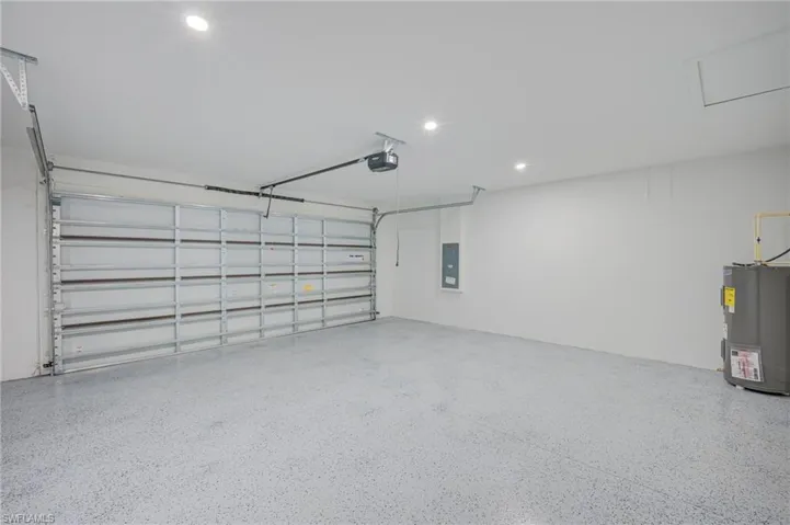 Finished garage featuring a speckled epoxy floor, recessed ceiling lighting, a metal sectional door with an automatic opener, and an integrated water heater