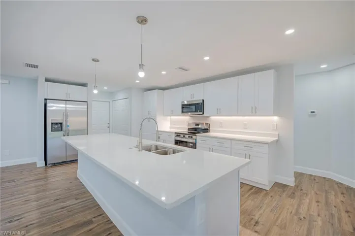 Kitchen featuring a central island with a dual-basin undermount sink, white cabinetry, integrated stainless steel appliances, and wood-finish flooring