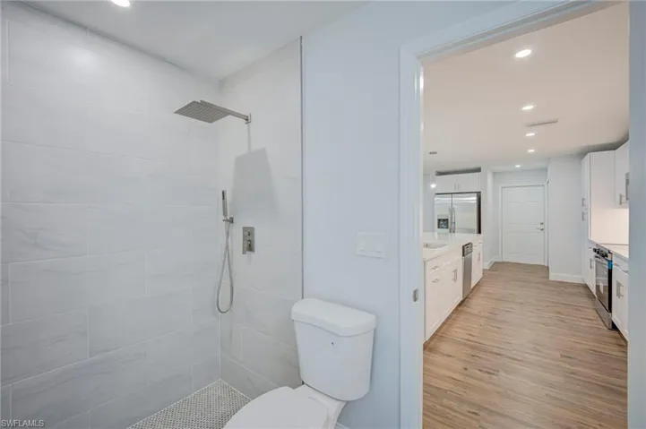 Walk-in shower featuring large-format porcelain tile, wall-mounted rainfall showerhead with handheld attachment, and penny-round tile flooring