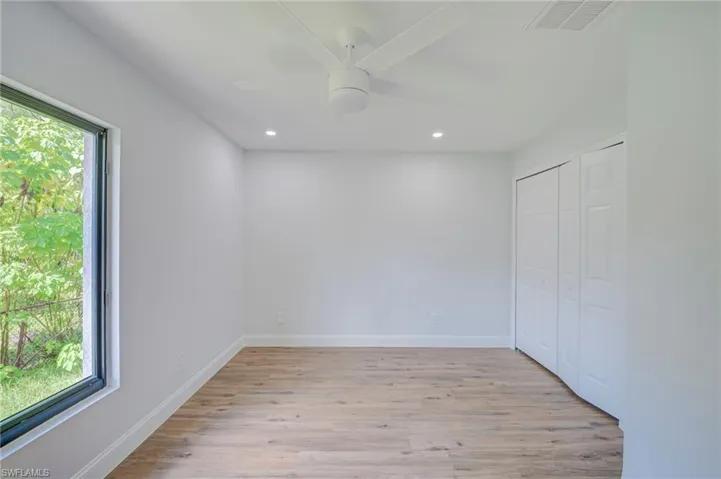 Room featuring wood-finish flooring, recessed lighting, a modern ceiling fan, a large window, and double-door closet cabinetry