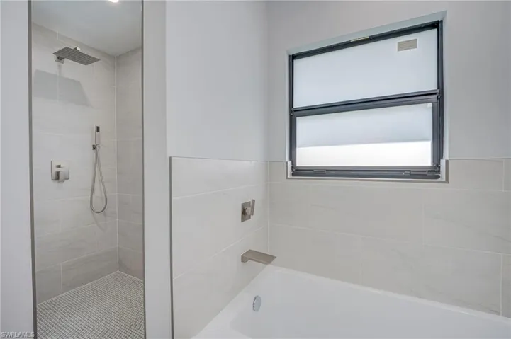 Bathroom featuring a combination soaking tub and walk-in shower with large-format wall tile, pebble-style floor tile, rain-style shower head, and brushed metal fixtures
