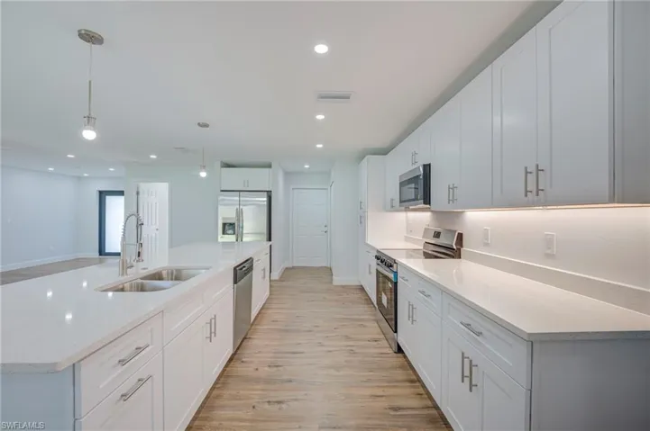 Kitchen featuring white cabinetry with nickel hardware, quartz countertops, stainless steel appliances, recessed lighting, and wood-finish flooring