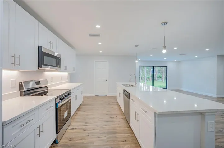 Kitchen featuring white cabinetry, solid-surface countertops, stainless steel appliances, a center island with an integrated sink, and wood-finish flooring