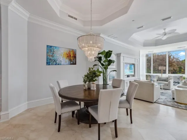 Dining area with a raised ceiling, crown molding, and ceiling fan with notable chandelier
