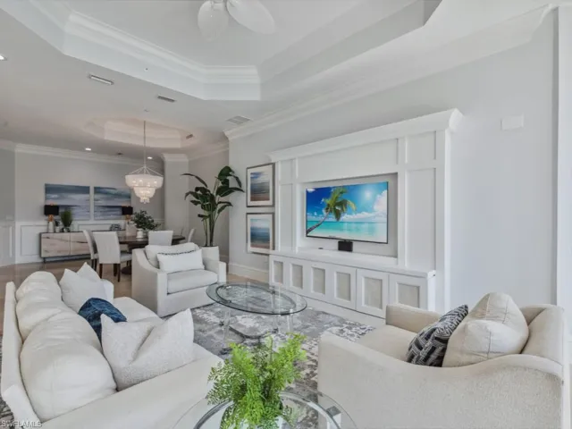 Living room with a tray ceiling, crown molding, and ceiling fan with notable chandelier