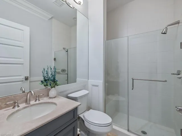 Bathroom with vanity, toilet, a shower with shower door, and crown molding
