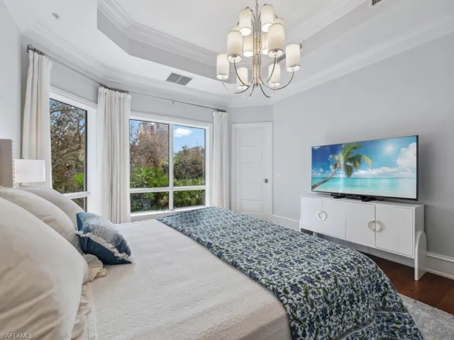 Bedroom with dark hardwood / wood-style flooring, ornamental molding, a tray ceiling, and an inviting chandelier