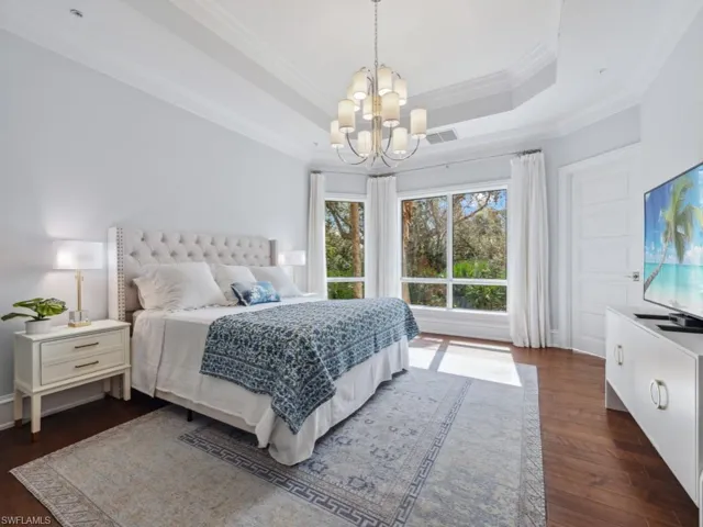 Bedroom featuring a tray ceiling, a notable chandelier, dark hardwood / wood-style floors, and ornamental molding