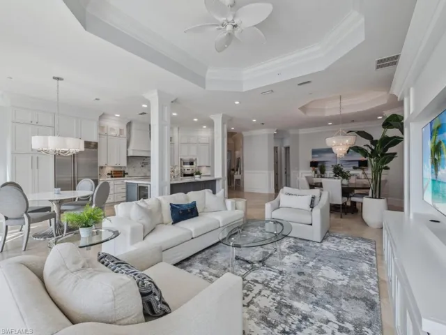 Living room with a raised ceiling, ornate columns, crown molding, and ceiling fan with notable chandelier