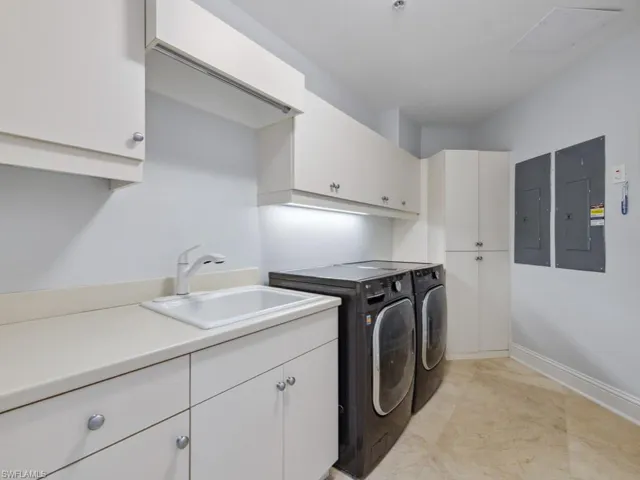 Laundry room featuring electric panel, sink, cabinets, and washing machine and dryer