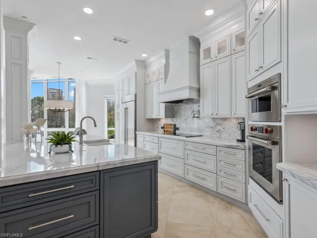 Kitchen with sink, decorative backsplash, white cabinets, custom exhaust hood, and appliances with stainless steel finishes