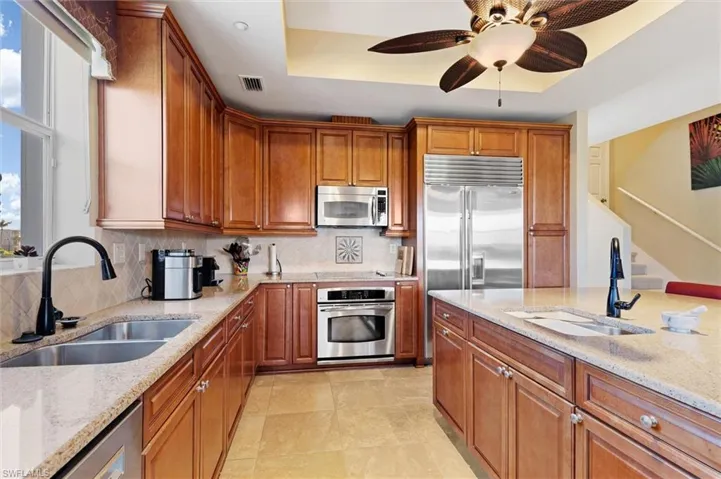 Kitchen with brown cabinetry, a raised ceiling, stainless steel appliances, and light stone counters