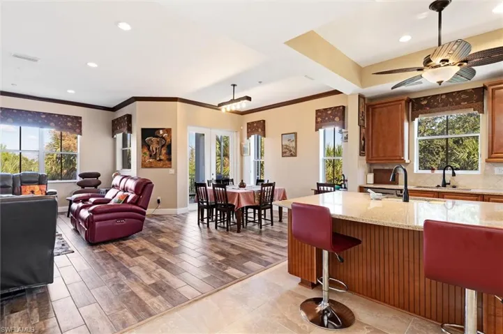 Kitchen featuring light stone counters, a breakfast bar, crown molding, brown cabinetry, and open floor plan
