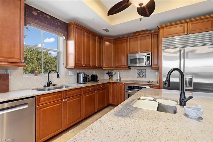 Kitchen featuring stainless steel appliances, brown cabinets, light stone countertops, and tasteful backsplash