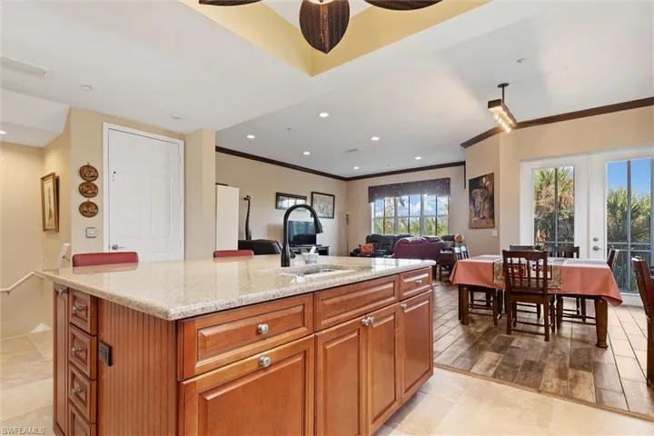 Kitchen featuring brown cabinetry, light stone countertops, a center island with sink, open floor plan, and ornamental molding