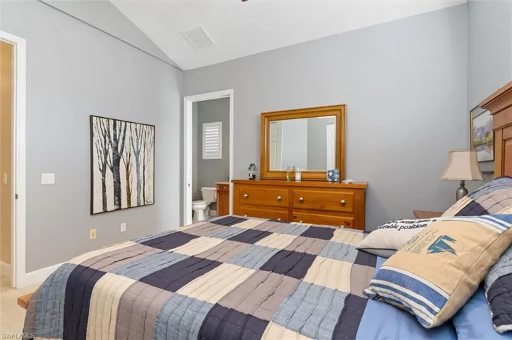 Carpeted bedroom featuring vaulted ceiling and ensuite bathroom