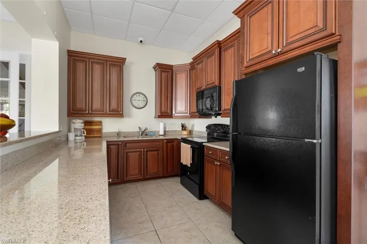 Kitchen featuring black appliances, a drop ceiling, light stone counters, light tile patterned flooring, and brown cabinets