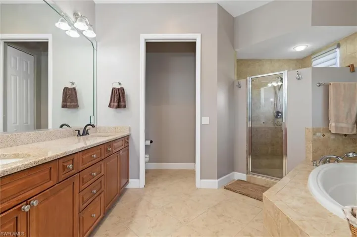 Full bathroom featuring a garden tub, double vanity, a shower stall, and light tile patterned floors