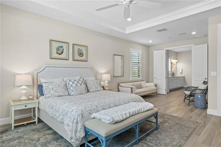 Bedroom featuring ornamental molding, wood-type flooring, ensuite bathroom, ceiling fan, and a raised ceiling