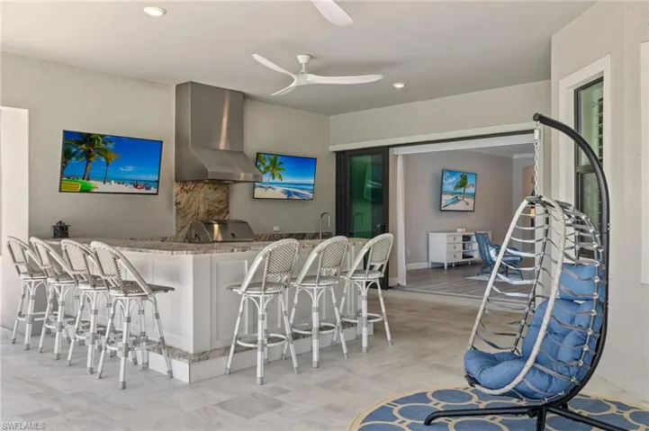 Kitchen featuring wall chimney range hood, light tile flooring, ceiling fan, and a kitchen bar
