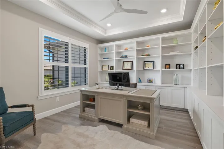 Home office with light hardwood / wood-style floors, crown molding, ceiling fan, and a raised ceiling