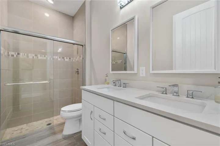 Bathroom with a shower with shower door, double sink vanity, and toilet