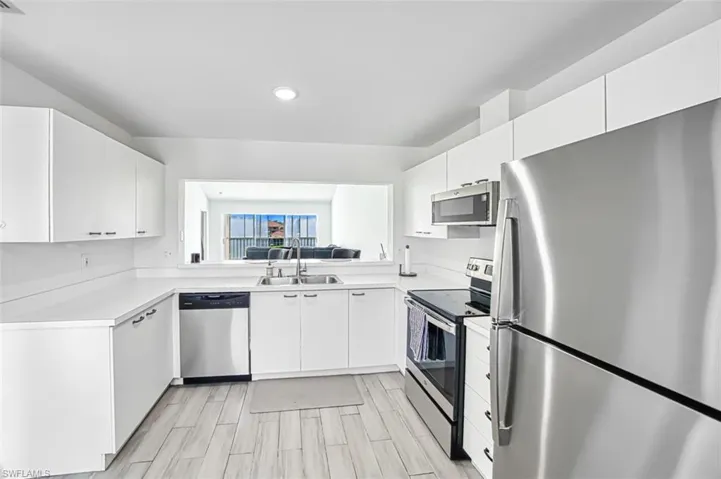 Kitchen featuring appliances with stainless steel finishes, light wood-type flooring, white cabinetry, and sink