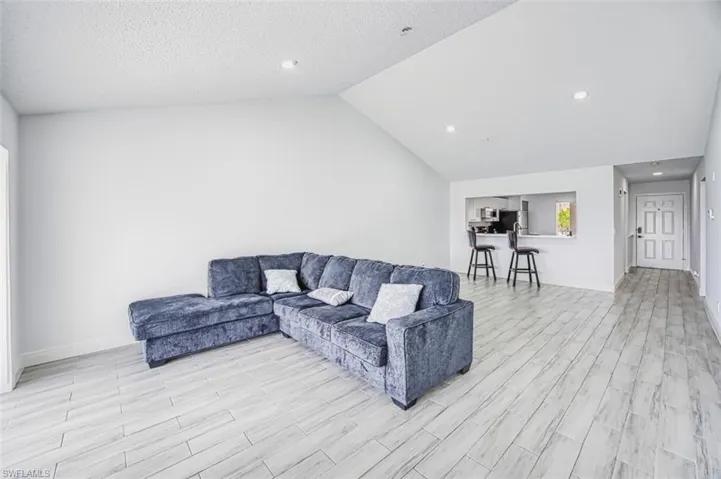 Living room with a textured ceiling, light hardwood / wood-style floors, and vaulted ceiling